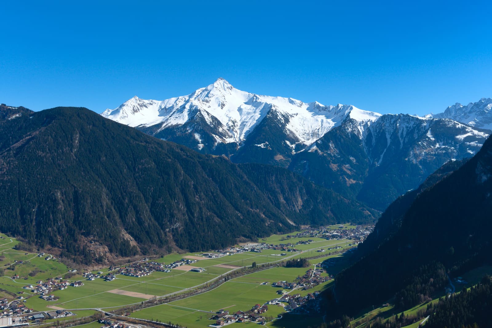 Het Zillertal met weiden en dorpen op de dalbodem en besneeuwde toppen erachter.